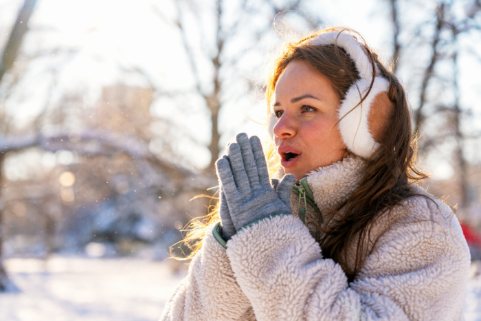 Frierende Frau im Winter mit Handschuhen und Ohrenschützern